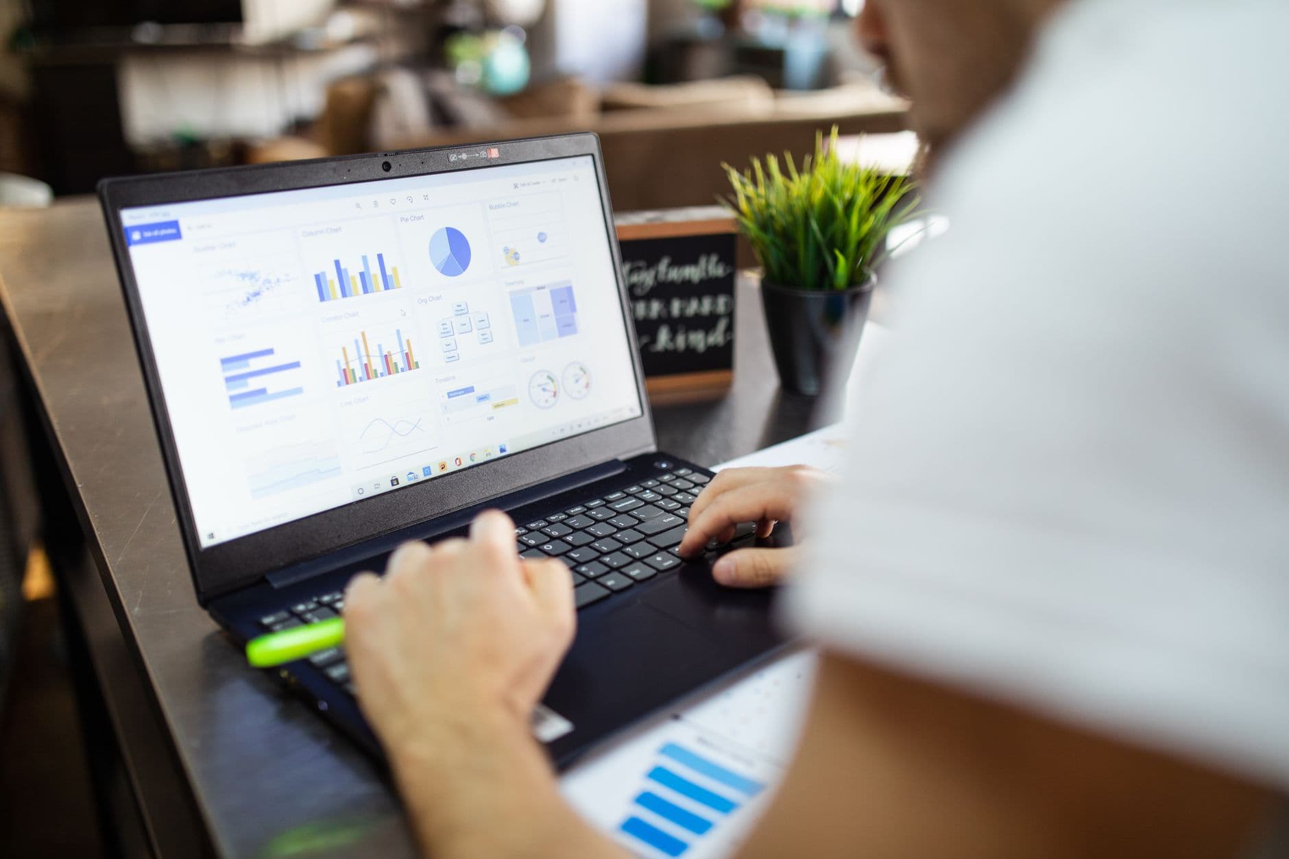 Laptop showing charts while someone reviews figures on paper