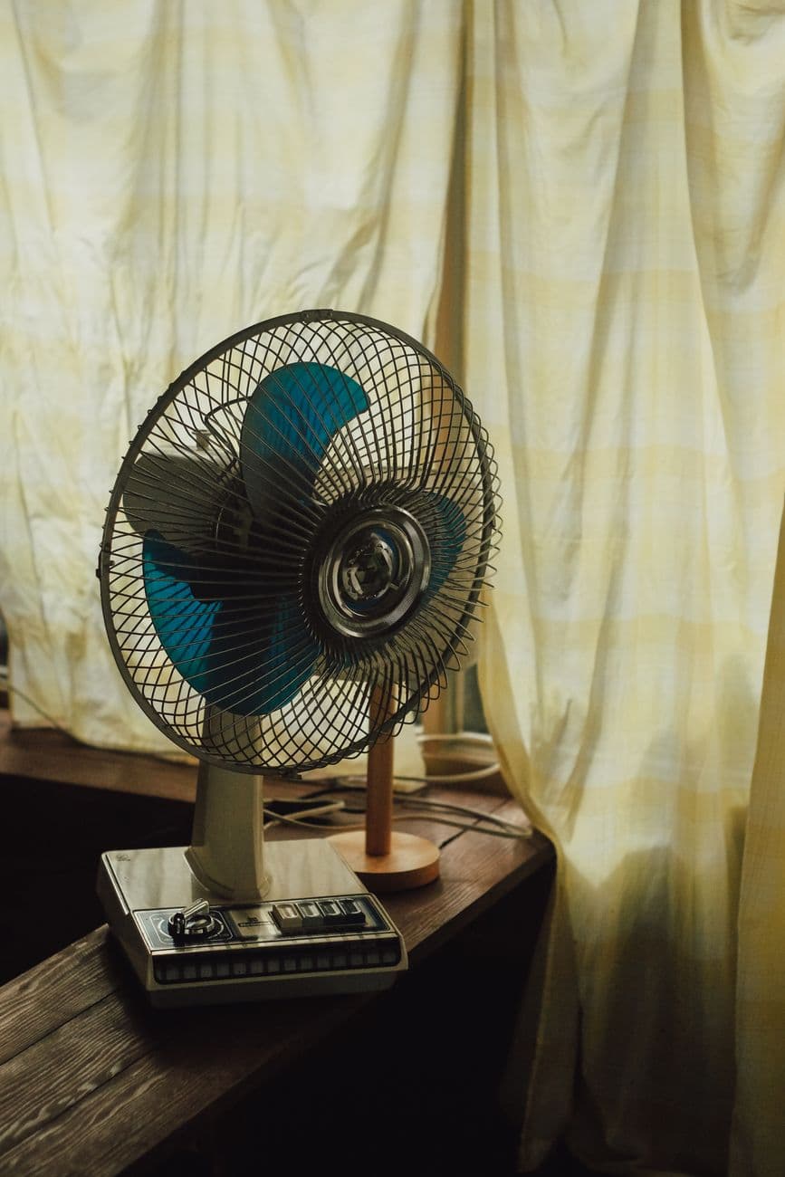 An electric fan beside sunlit curtains in a warm room