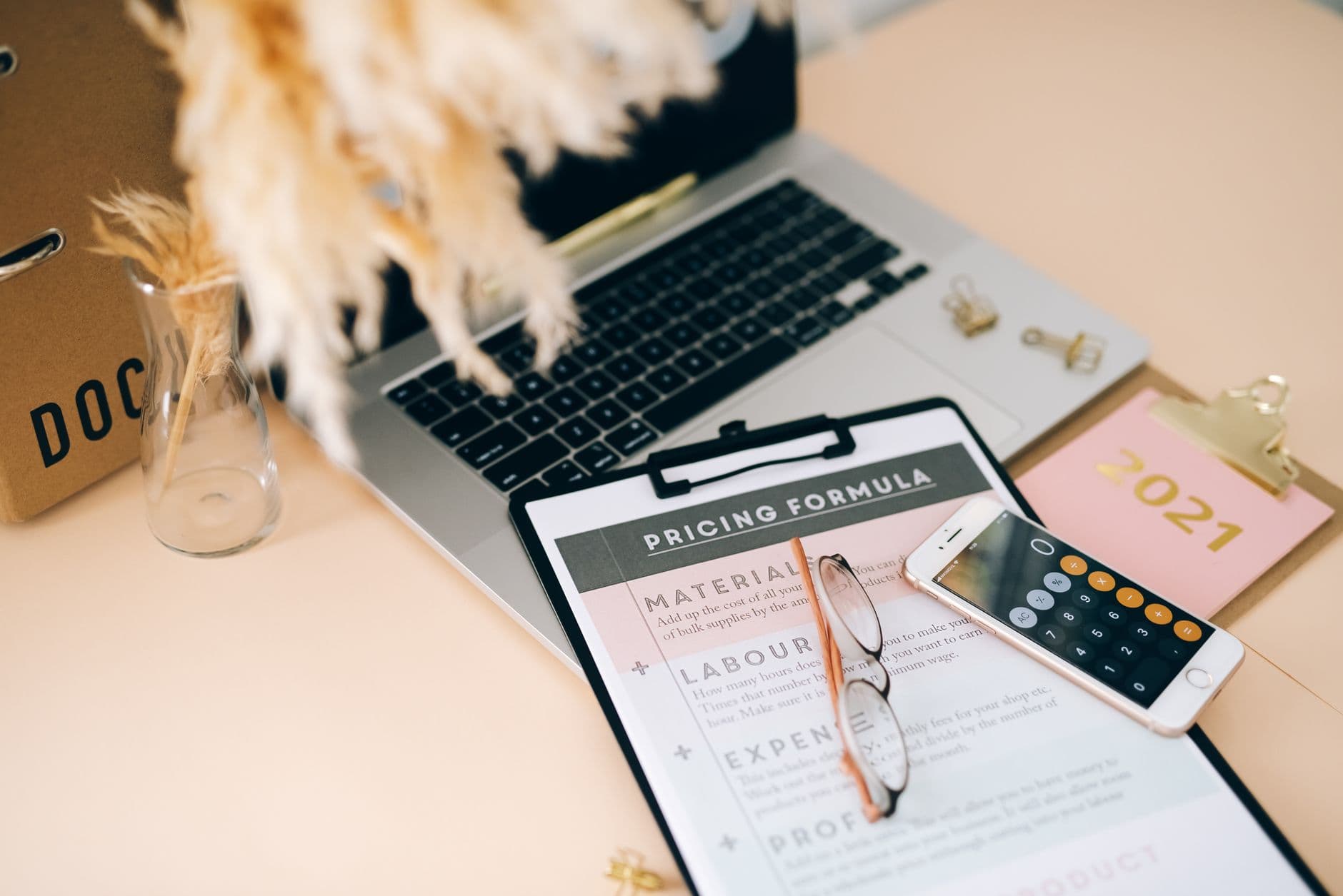 Desk with a pricing worksheet, laptop, and smartphone calculator used to plan nightly rates