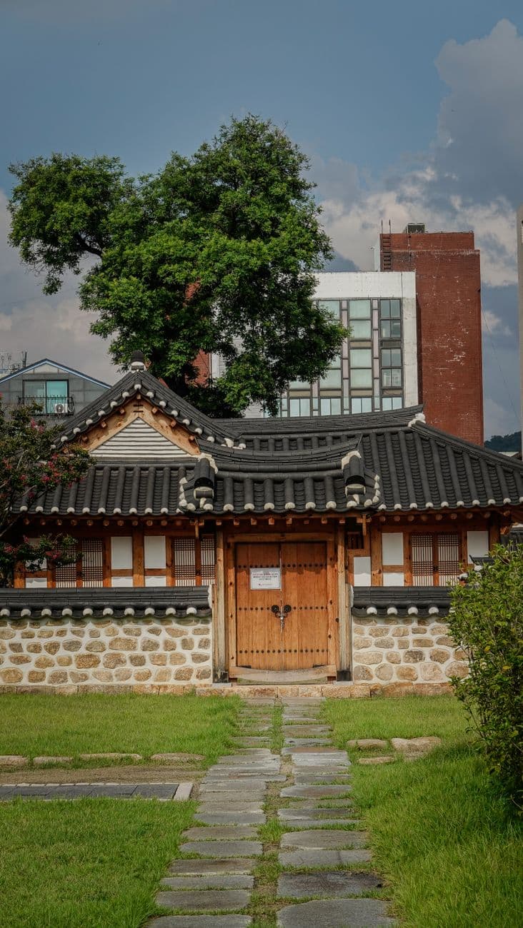현대식 도시 건물을 배경으로 자리한 한옥 주택 — 도시 속 주택에서 외국인 게스트를 맞는 도시민박업의 풍경